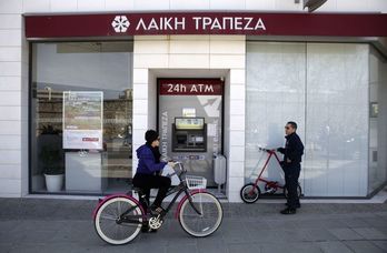 Una mujer pasa con su bici ante una sucursal bancaria. (Yiannis KOURTOUGLU/AFP PHOTO)