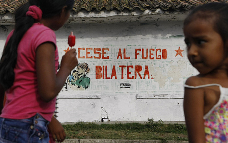 Bi haur FARCen eta Kolonbiako Gobernuaren arteko su-etenari buruzko mural baten aurrean